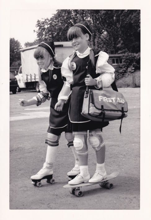 A black and white photograph of two young girls, both St John Ambulance ‘Badgers’, one on a skateboard and one on rollerskates. It is a publicity photograph for the launch of the Badger Safety Week initiative, and the two girls are holding first aid equipment.