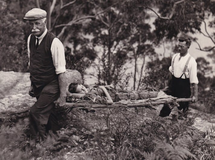 A black and white photograph of two men carrying a simulated patient on a homemade stretcher.
